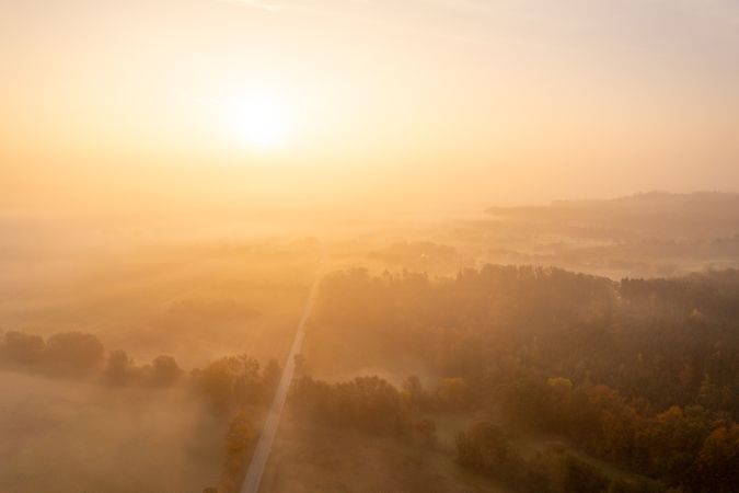 Aerial image with multicolored forest and a road on a foggy morning of autumn