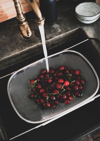 Cherries being washed in strainer over kitchen sink