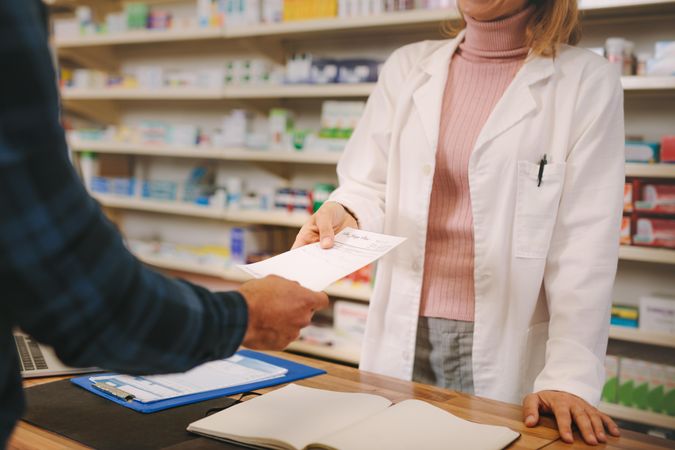 Cropped shot of customer handing a prescription to the female pharmacist