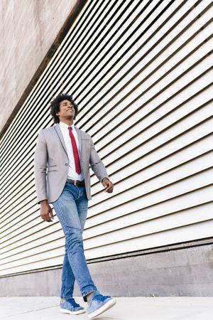 Man in jeans and dress shirt with tie walking next to wall