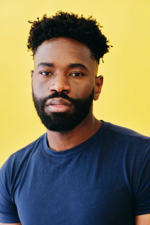 Portrait of Black man in navy t-shirt in yellow studio