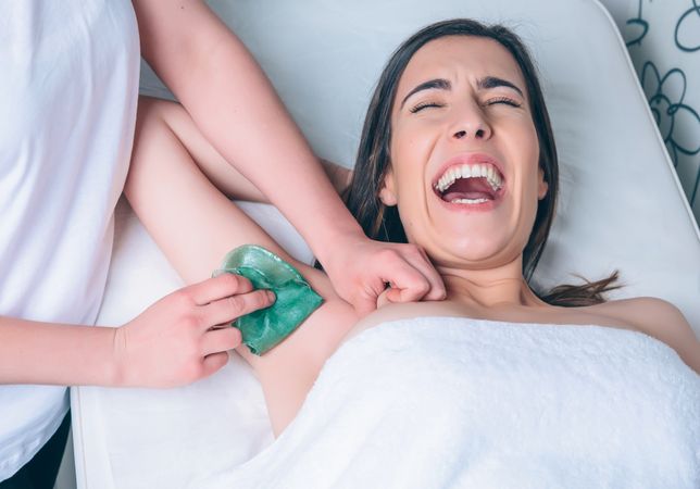 Aesthetician's waxing grimacing woman's armpit in a beauty salon
