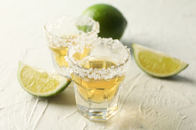 Tequila shots with salt and lime slices on light background