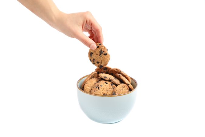 Young woman holding tasty chocolate chip cookie over bowl on studio background, closeup
