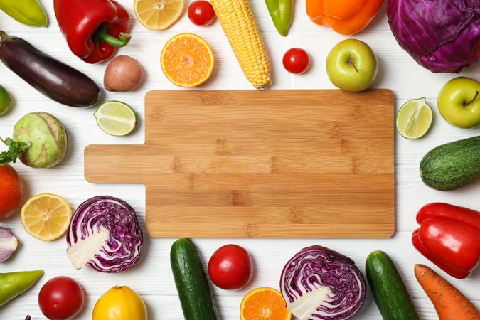 Board and different vegetables and fruits on wooden background, top view