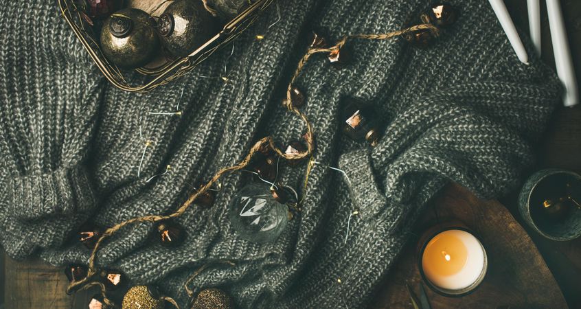 Festive decorations, garland and candle arranged around a woolen sweater