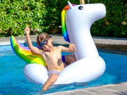 Positive child sitting on inflatable unicorn in outdoor swimming