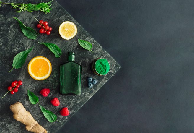 Healthy scene of spirulina powder, nettle leaves, berries, ginger on marble slap on dark background