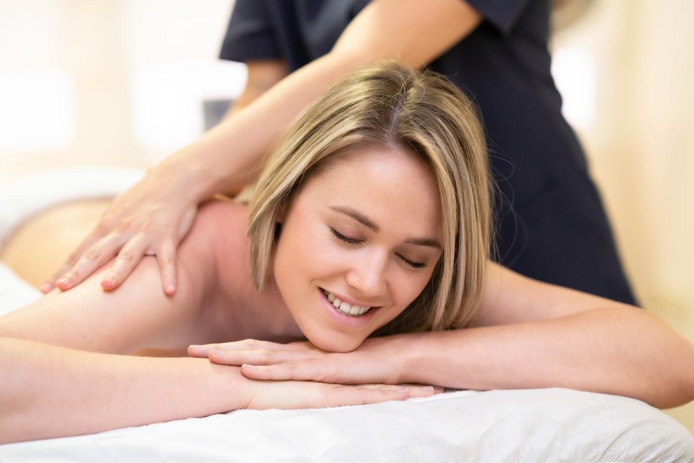 Smiling blonde female having shoulders massaged on the table