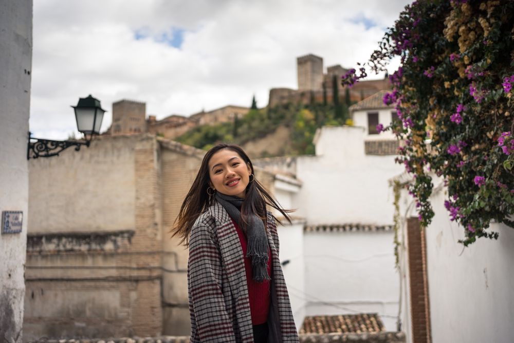 Asian female traveler in warm wear smiling among old buildings near big castle