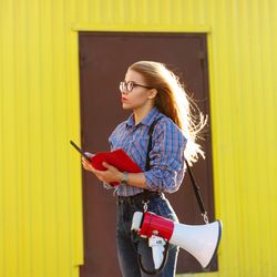 Side view of woman taking notes dressed in checkered shirt against a yellow wall