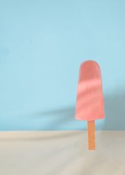 Pink ice pop on blue background with sand
