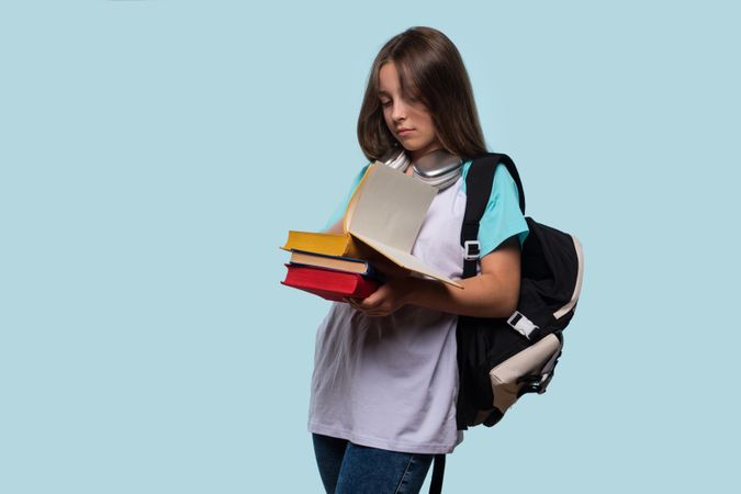 Serious girl reading book while holding multiple books