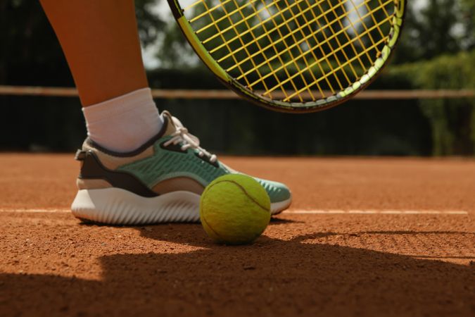 Woman leg, racket and tennis ball on clay court