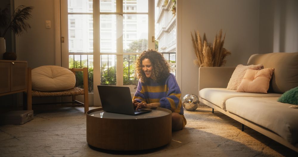 Portrait of Smiling Young Woman Working from Home on Laptop Computer in Sunny Apartment.