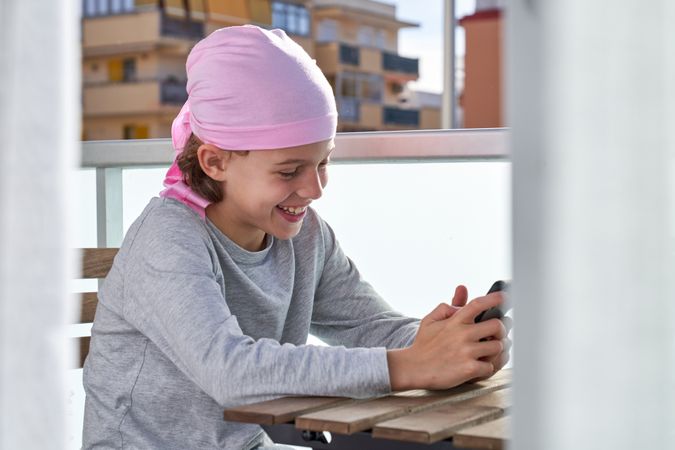 Cheerful child in pink bandana browsing phone on terrace