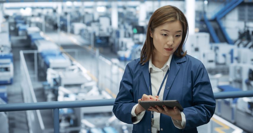 Portrait of a Japanese Engineer Using Tablet Computer and Looking Around a Factory Facility with Equipment Producing Modern Electronic Components for Different Industries