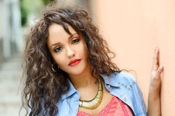 Female with long curly hair outside next to beige wall