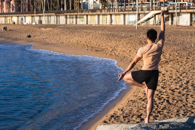 Shirtless man balancing in yoga pose on beach