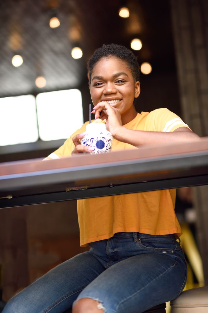 Happy female sitting with ice tea at counter of modern cafe