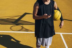 Male basketball player using his smartphone resting after training