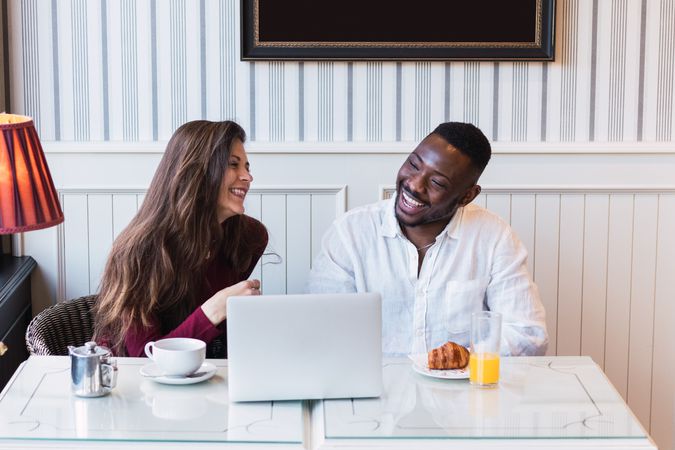 Cheerful multiethnic couple using laptop during breakfast at home