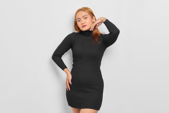 Serious Asian woman with red hair, hand on hip and turtle neck dress in studio
