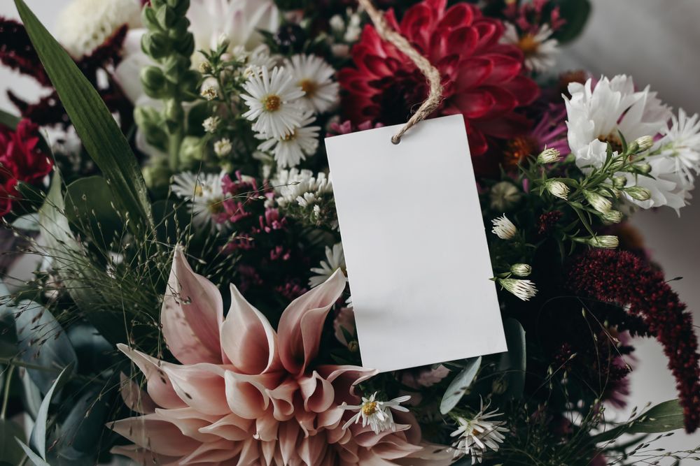 Closeup of blank paper card, gift tag label on colorful pink and burgundy dahlias, cosmos and aster flowers