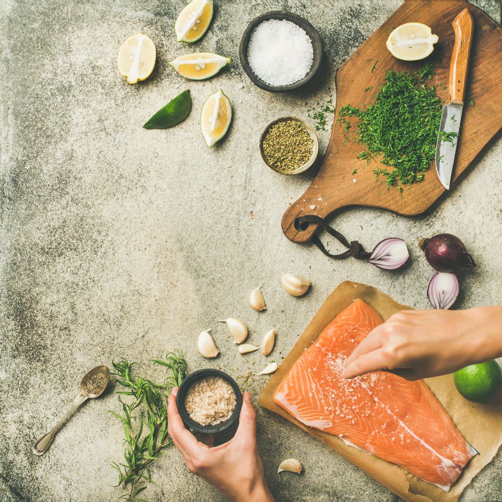 Salted salmon fillet with fresh herbs, limes, onions, bread board, hand with salt, copy space