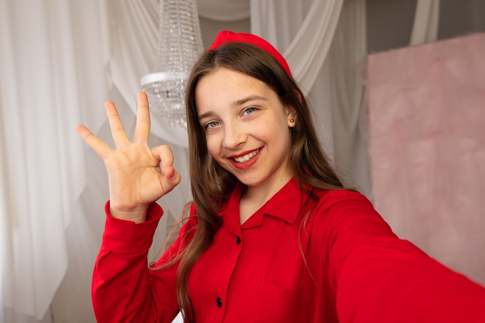 Teen girl smiling taking selfie showing okay hand gesture...