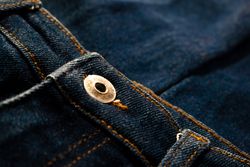 Close up gold and shiny button navy blue jeans fabric background texture.
