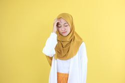 Stressed Asian Young Woman in White Shirt and Mustard Veil Touching his Head and Having Headache.