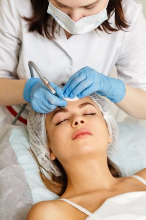Woman having facial beauty treatment with instrument above her eyebrows, vertical