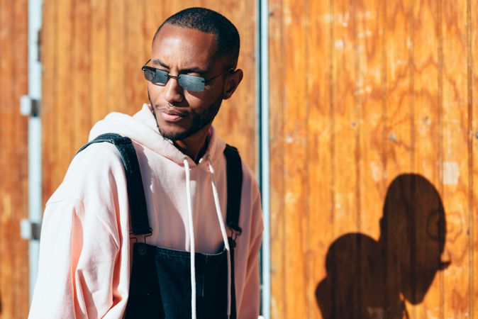 Male wearing overalls looking around by a wooden wall