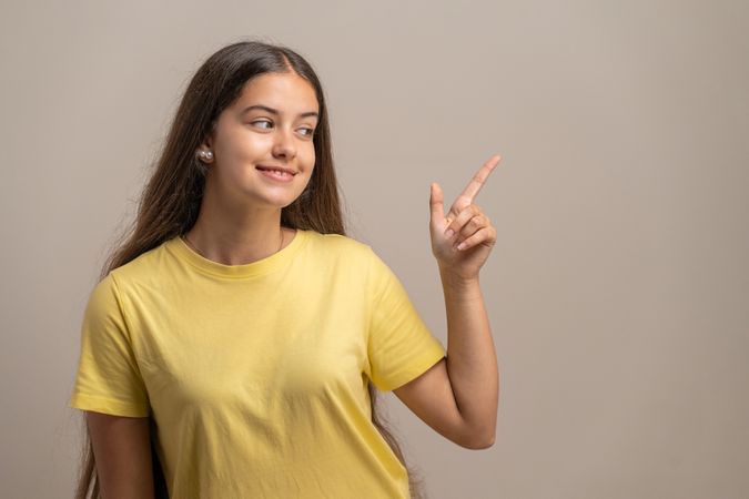 Young woman with a pleasant smile, looking and pointing to the side.