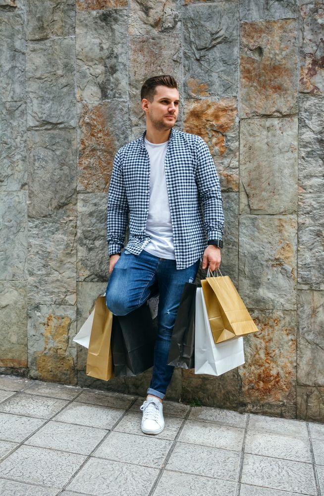 Young man with shopping bags leaning on wall
