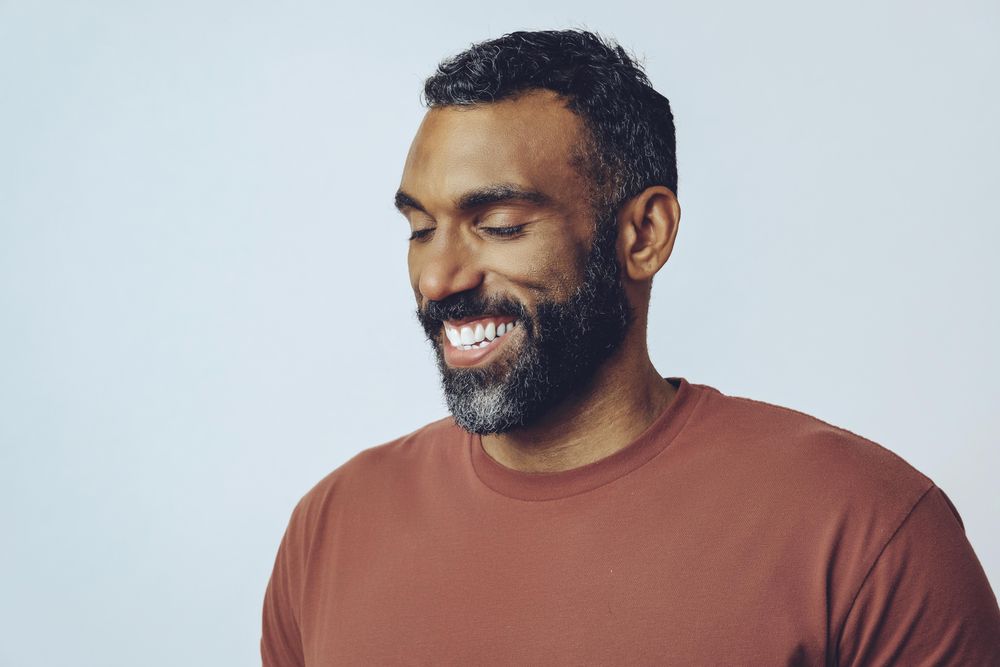 Portrait of smiling Black male looking at ground in grey studio