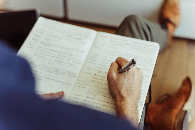 Close up of a man’s hand holding a pen and writing in a diary