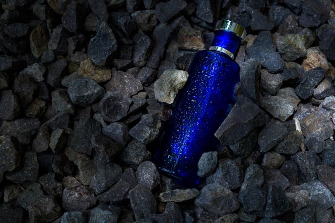Blue perfume bottle mock up laying in rocky terrain with copy space