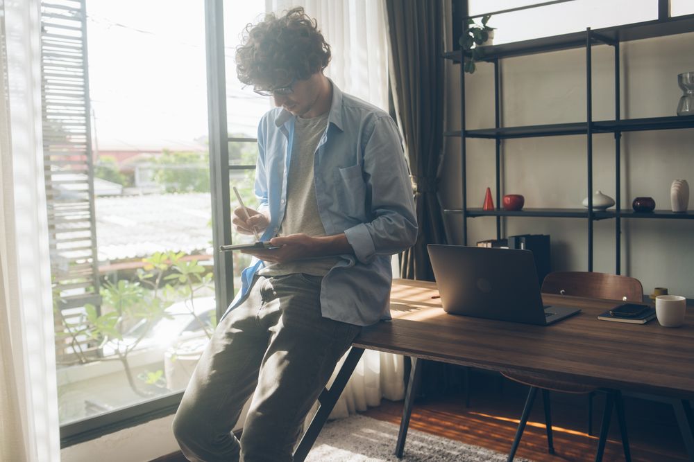 Creative designer writing on digital tablet while casually sitting on desk at home