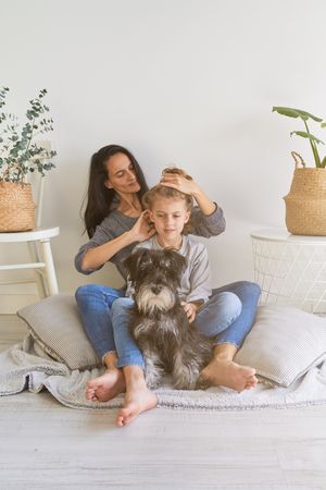 Mother doing hairstyle to son near dog
