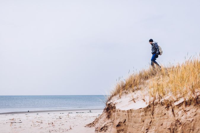 Man walking on sand shore between dry grass near water