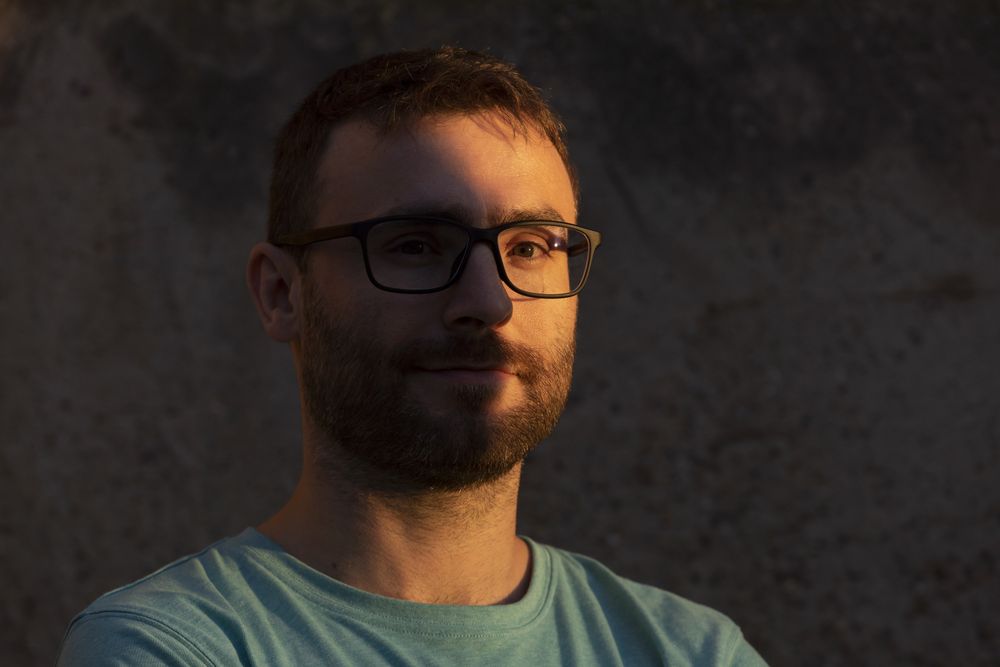 Portrait of a man looking at the camera, with beard and glasses in the shadows of the sunset
