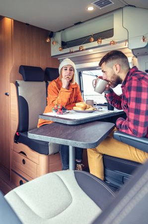 Male and female friend enjoying breakfast rolls and coffee in back of van, vertical