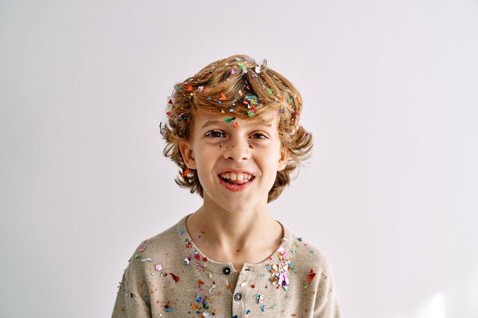 Delighted boy with curly blond hair and covered with confetti