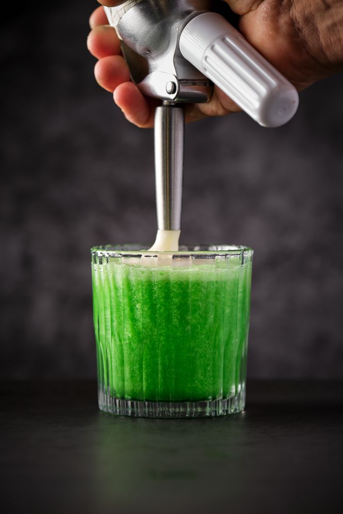 Crop bartender adding whipped foam to delicious cocktail with cr