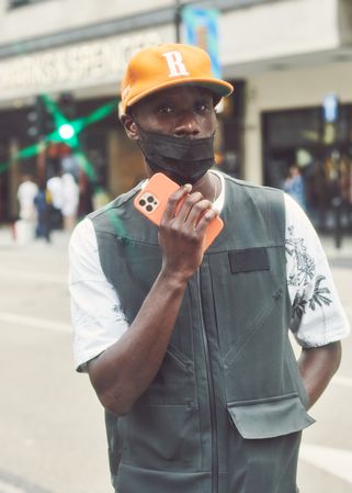 London, England, United Kingdom - September 18 2021:Man with orange cap and phone with facemask