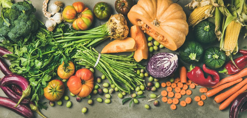 Fresh produce on concrete background, with halved squash, corn, cabbage, wide composition