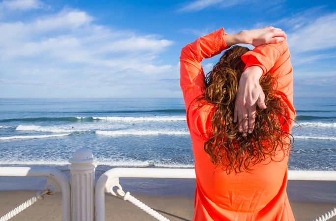 Back of fit woman stretching triceps before workout on the beach promenade