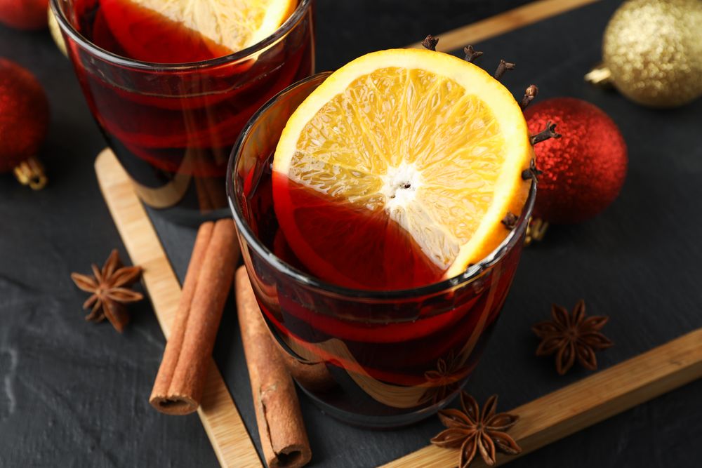 Glasses of tasty mulled wine and christmas baubles on dark background, close up